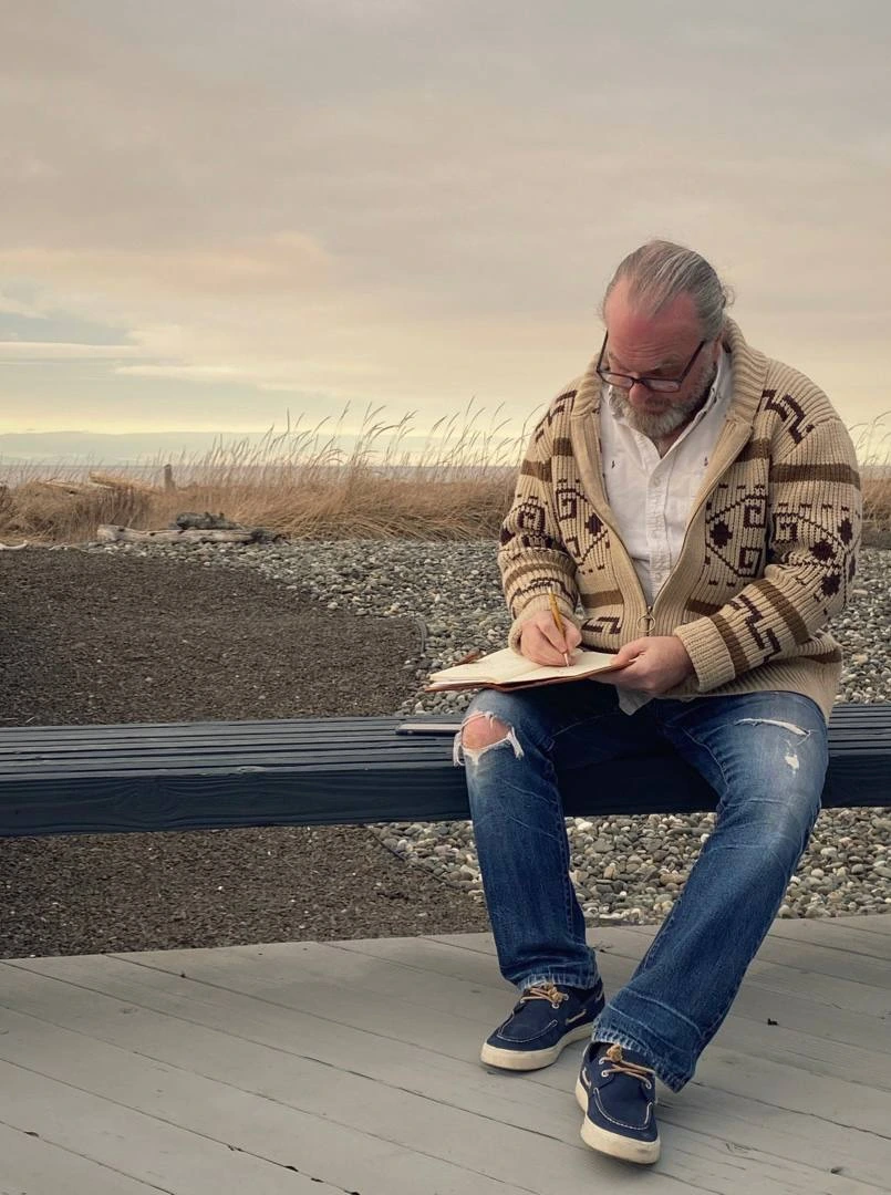 Jonathan Quinn Barnett sketching outdoors beside the shore, with pencil, hands and sketchbook visible.